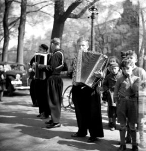 Kinderen rond een groep straatmuzikanten in Volendams kostuum met accordeons, Bestanddeelnr 254-2322