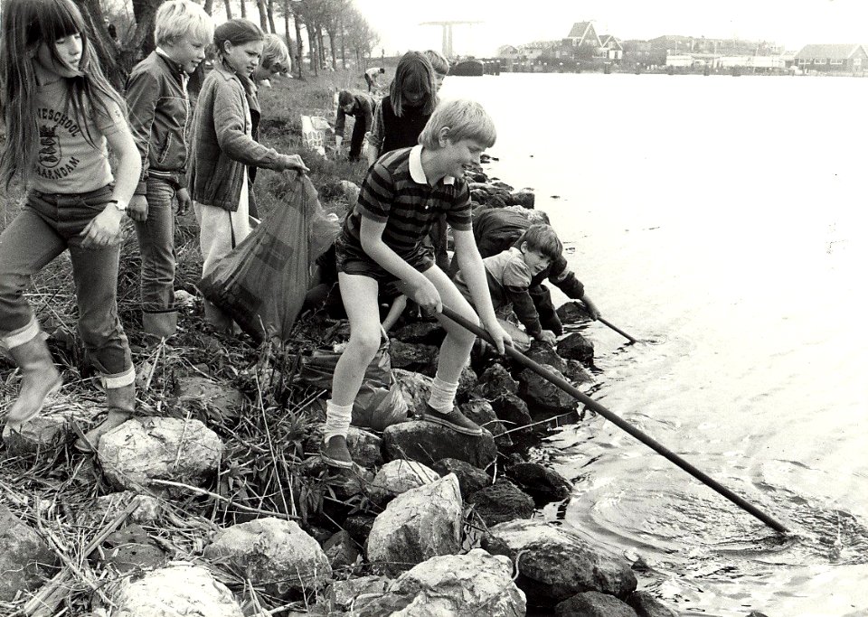 Kinderen die een grote schoonmaakactie houden in Zijkanaal C. Aangekocht in 1983 van fotograaf C. de Boer. - Negatiefnummer 23004 k 21 a. - Gepubliceerd in het Haarlems Dagblad van 27.04.198, NL-HlmNHA 1478 25900 K 38