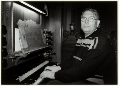 Kerkorganist Willem Wijting op zijn favoriete plek in de Nieuwe Kerk, aan het Hessvan Covelen-orgel. Toen hij 25 jaar verbonden was aan de Nieuwe Kerk, werd hij onderscheiden met het zilver, NL-HlmNHA 54037059
