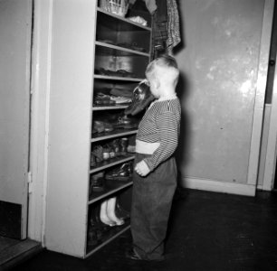 Kleuter met een paar schoenen in de hand bij een kast vol schoenen, Bestanddeelnr 252-9101