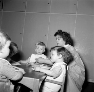 Kleuters zitten aan tafeltjes te eten onder begeleiding van de leidsters, Bestanddeelnr 252-9095