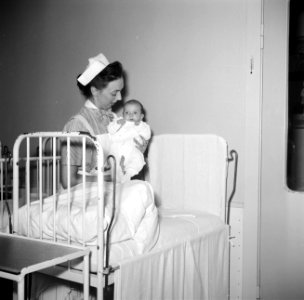 Kinderverzorgster met een baby bij een ledikantje, Bestanddeelnr 252-9110 photo