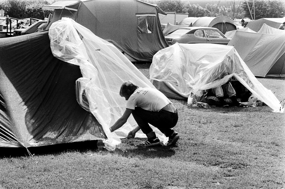 Kampeerders bedekken tenten met plastic tegen de regen op een Amsterdamse campin, Bestanddeelnr 930-3830