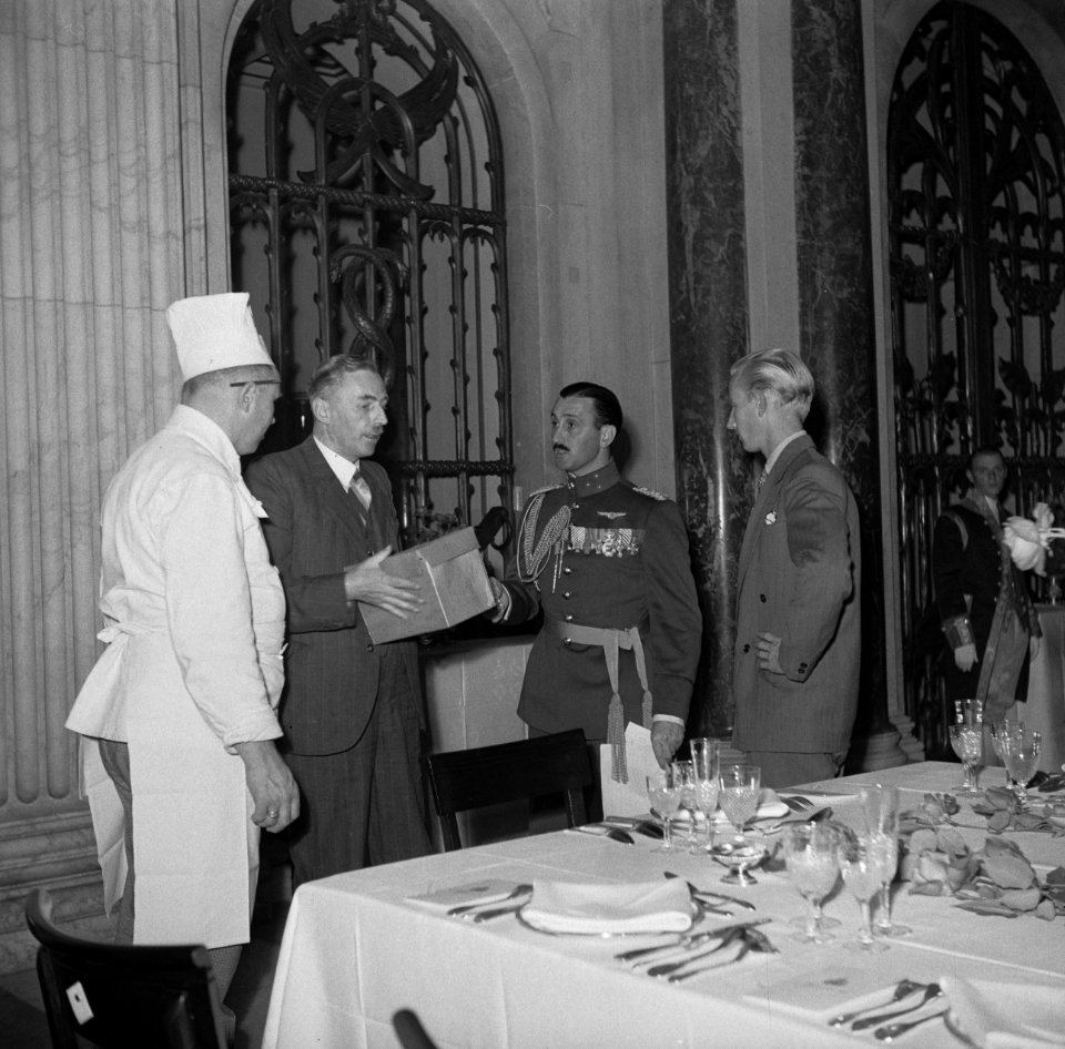 Kapitein in gala-uniform in besperking met twee heren in burger en een kok in h…, Bestanddeelnr 935-3485