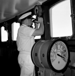 Kapitein in wit uniform met verrekijker in de stuurhut staande bij de scheepstel, Bestanddeelnr 255-4954
