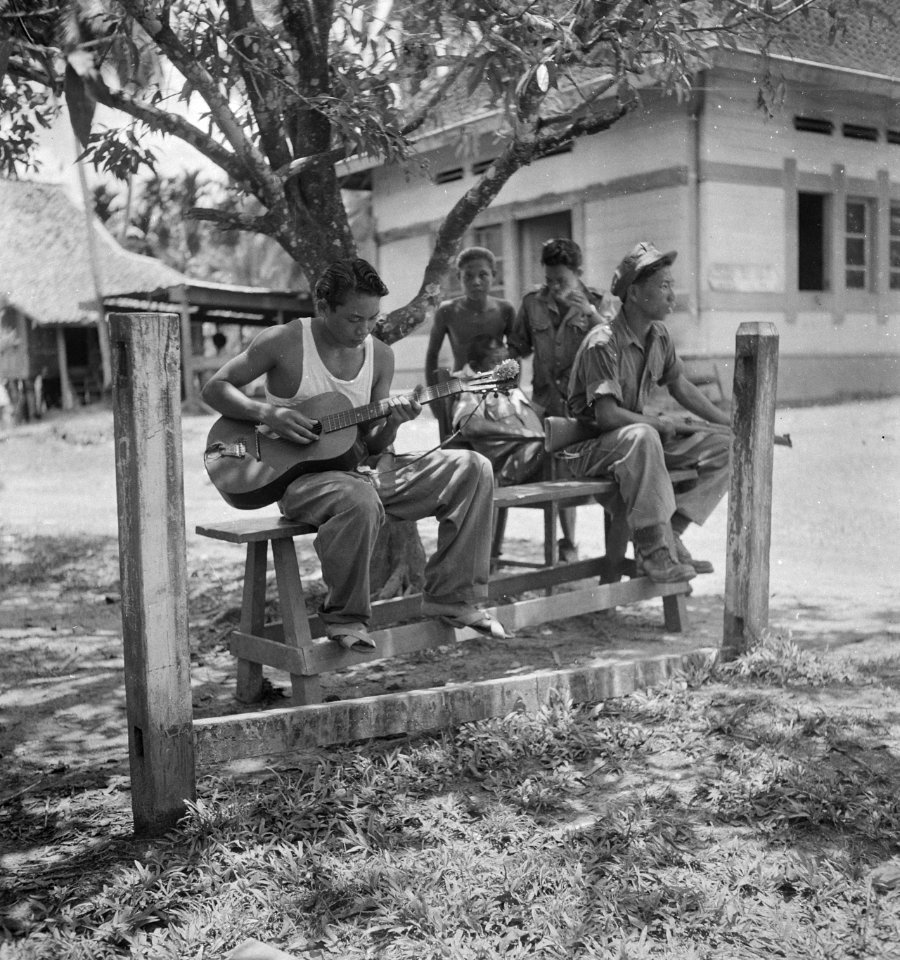 KNIL-militairen tijdens een rustpauze. Een militair speelt gitaar, Bestanddeelnr 13211