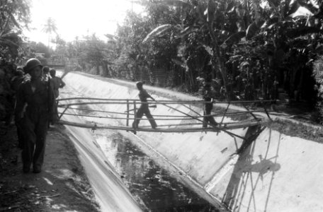 KNIL-militairen passeren een bamboe loopbrug over een afwateringskanaal, Bestanddeelnr 6467