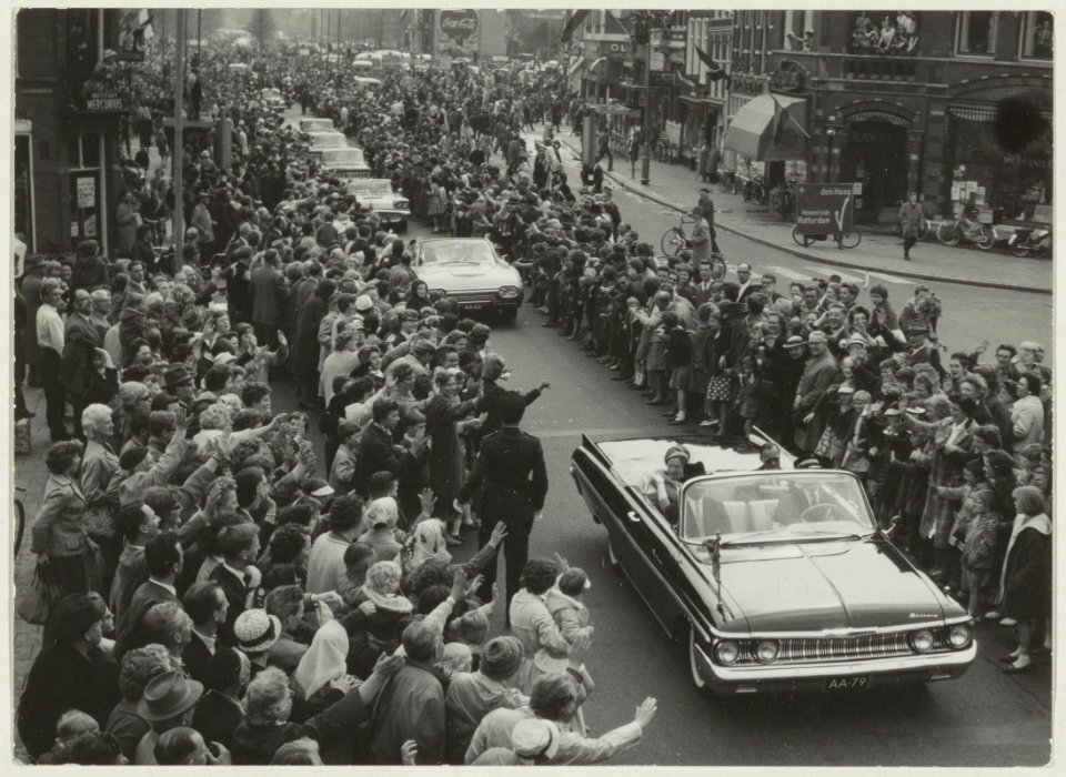 Koninklijk bezoek aan Haarlem. In de auto voorgrond Koningin Juliana en Prins Bernhard, daarachter de auto met de prinsessen op het Houtplein. NL-HlmNHA 54011215