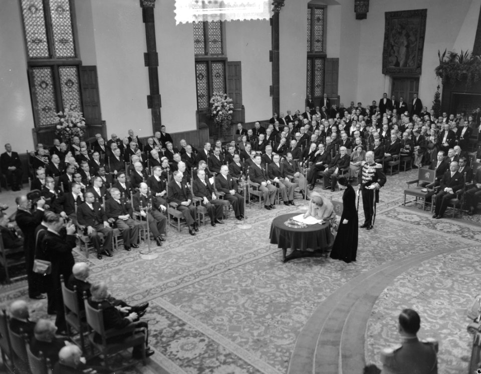 Koningin Juliana ondertekent de Acte van Besvestiging. Naast haar de Directeur v, Bestanddeelnr 906-8921