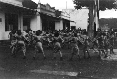 Leden Vrouwenkorps KNIL dansen in een reidans om een boom en een vlaggemast heen, Bestanddeelnr 220