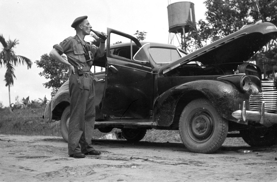 Legerfotograaf (met de rang van onderluitenant KNIL) drinkt uit een fles staande, Bestanddeelnr 5592