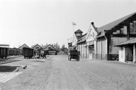 Legertruck rijdt langs spoorwegemplacement. Rechts aan een loods hangt de Nederl, Bestanddeelnr 285-2-2