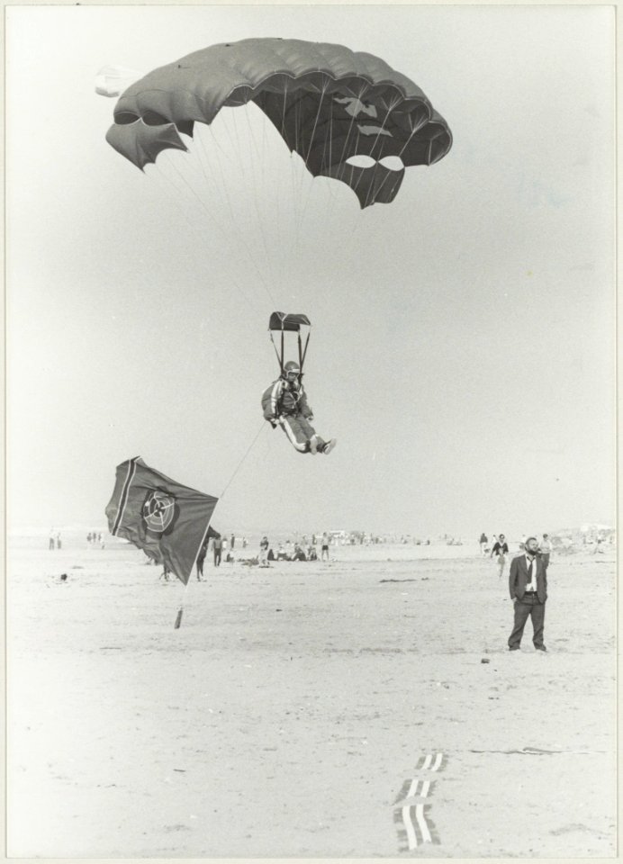 Landing op het strand van een parachutist met een reclamevlag van het casino. NL-HlmNHA 54013124