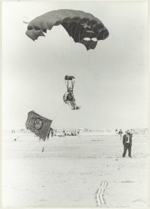Landing op het strand van een parachutist met een reclamevlag van het casino. NL-HlmNHA 54013124