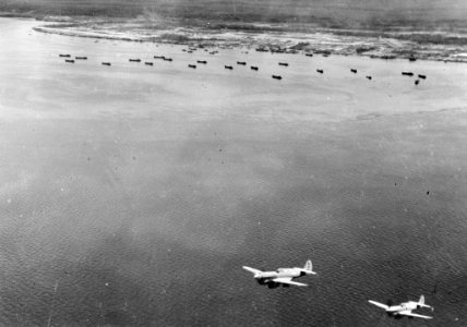Luchtfoto. Landingsvaartuigen aan de kust. Onderin vliegen twee jachtvliegtuige, Bestanddeelnr 8271