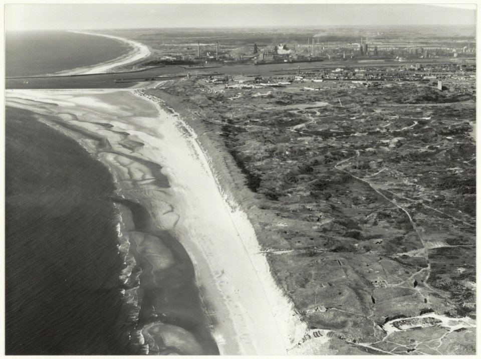 Luchtfoto van de kustlijn tussen Bloemendaal aan Zee en Egmond aan zee met de door de gewijzigde stroming onstane strandvlakte bij de Zuidpier. Rechts boven het midden IJmuiden en de staalfa, NL-HlmNHA 54015677