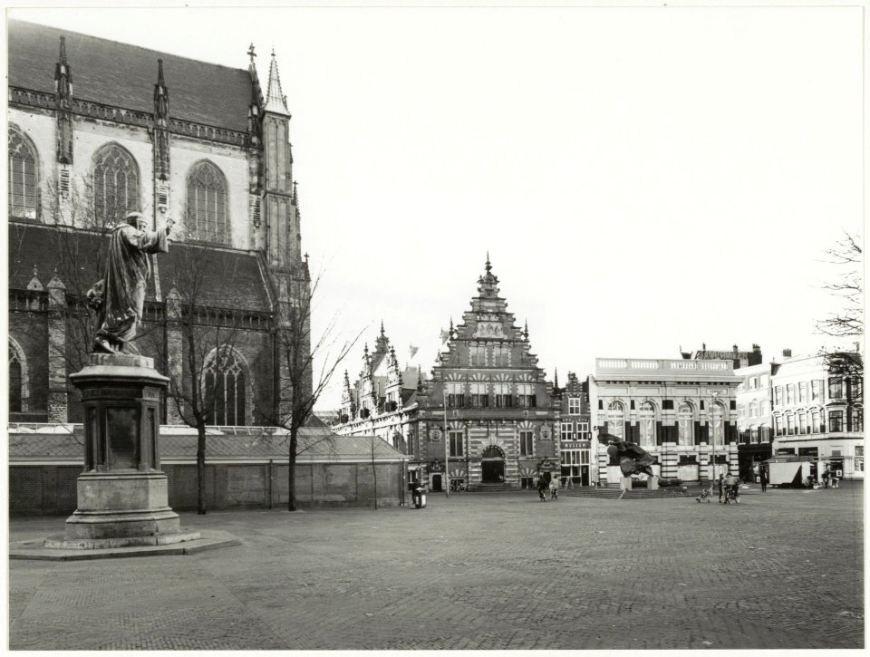 Links op de foto het standbeeld van Laurens Janszoon Coster, daarachter de Grote of St. Bavokerk, in het midden de Vleeshal, rechts daarvan het Verweymuseum. Rechts in het midden het beeld , NL-HlmNHA 54037584