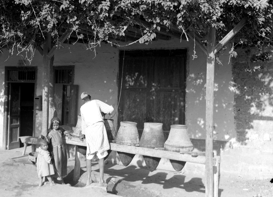 Man en kinderen bij stenen kruiken voor een woonhuis, Bestanddeelnr 191-0097