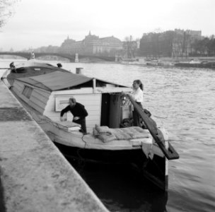 Man en vrouw aan het werk in de kuip van een woonboot die is afgemeerd aan een k, Bestanddeelnr 252-9393
