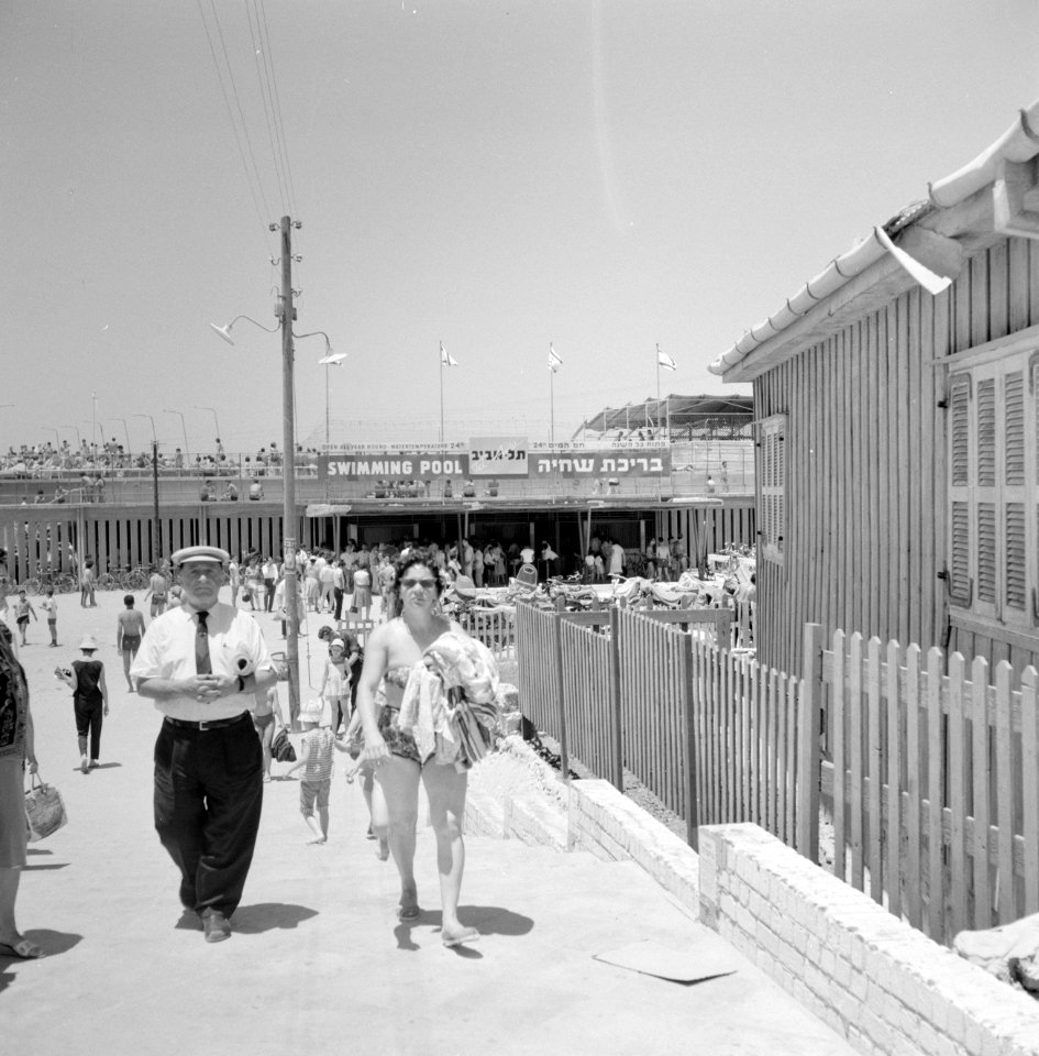 Man en vrouw lopen weg van een druk plein dat toegang geeft tot het strand, Bestanddeelnr 255-1937