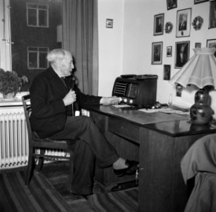 Man zit met een pijp aan een bureau met daarop een radio voor het raam te roken, Bestanddeelnr 252-9128