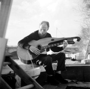 Man bespeelt een snaarinstrument aan dek van het schip Siegfried & Erik te Parij, Bestanddeelnr 252-9424