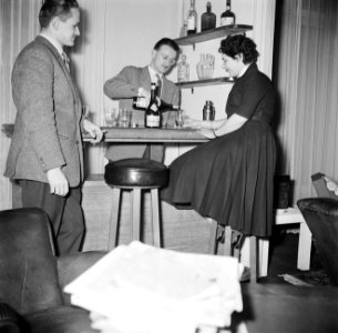 Man achter zijn huisbar terwijl hij een dame een glas alcohol inschenkt naast h, Bestanddeelnr 252-9369