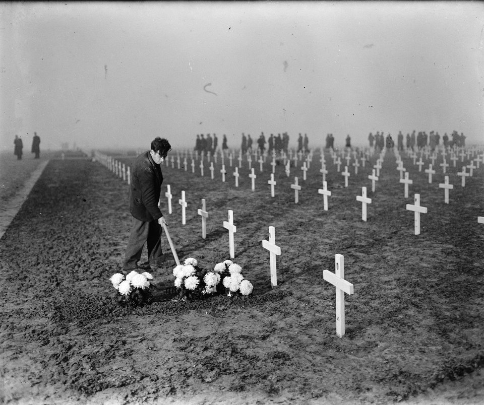 Man schoffelt bij een graf waar bloemen zijn gelegd, Bestanddeelnr 900-0421