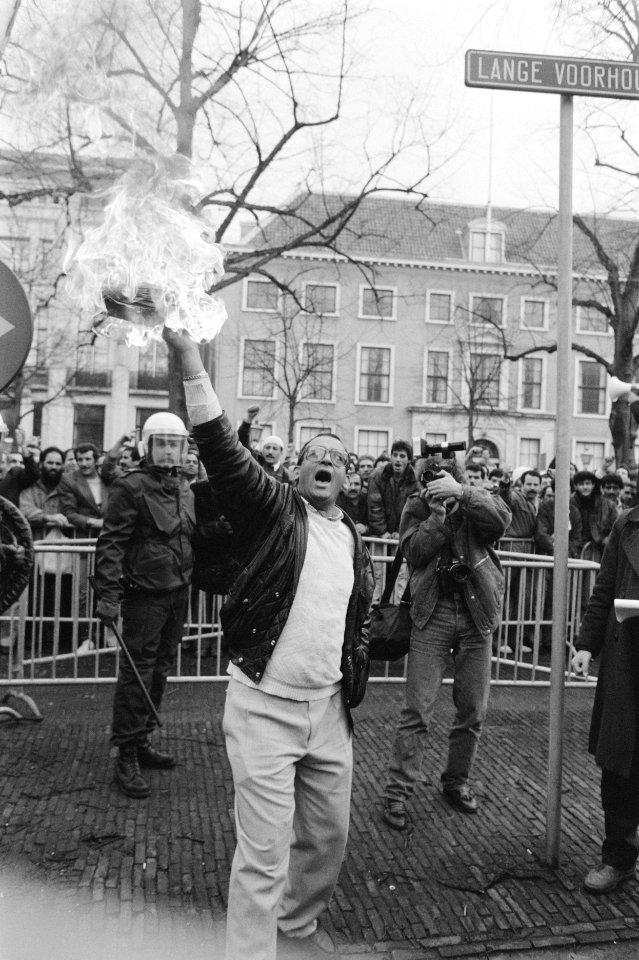 Man met brandend boek en daarachter iemand van de Mobiele Eenheid en een fotogra, Bestanddeelnr 934-4146