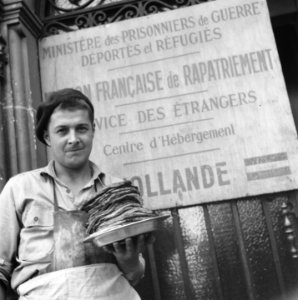 Man met schaal met pannenkoeken staat voor een uithangbord van een Frans repatri, Bestanddeelnr 900-5906 photo