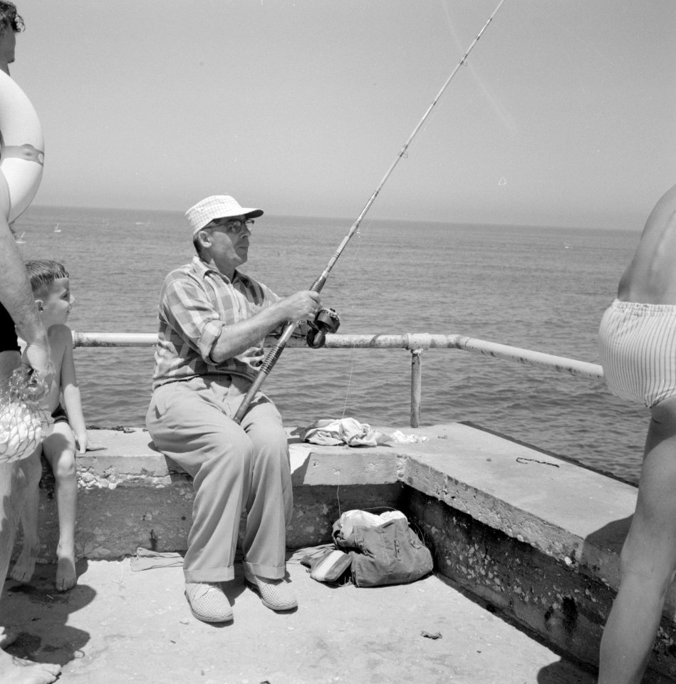 Man aan het vissen in zee terwijl een kleine jongen toekijkt, Bestanddeelnr 255-1962