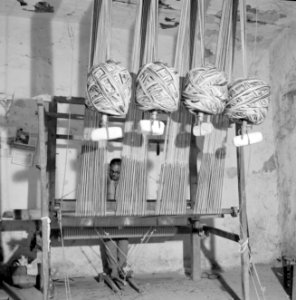 Man aan een weefgetouw Op de voorgrond knotten draad waaraan gewichten hangen, Bestanddeelnr 255-4454