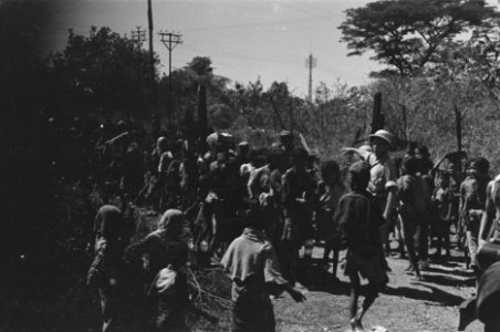 Man met tropenhelm wijst. Om hem heen een grote groep kinderen en vrouwen, Bestanddeelnr 346-2-2