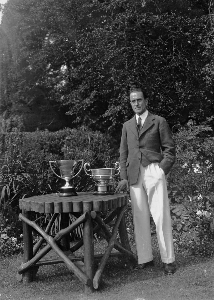 Man standing next to a garden table on which are two golfing trophies (1293610)