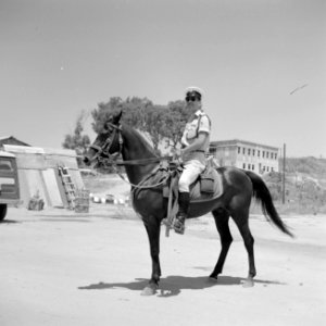 Mannelijke agent te paard, op de achtergrond een bouwvallige omgeving, Bestanddeelnr 255-2021 photo