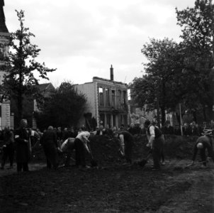 Mannen graven onder toezicht van een man met een armband, Bestanddeelnr 900-3007