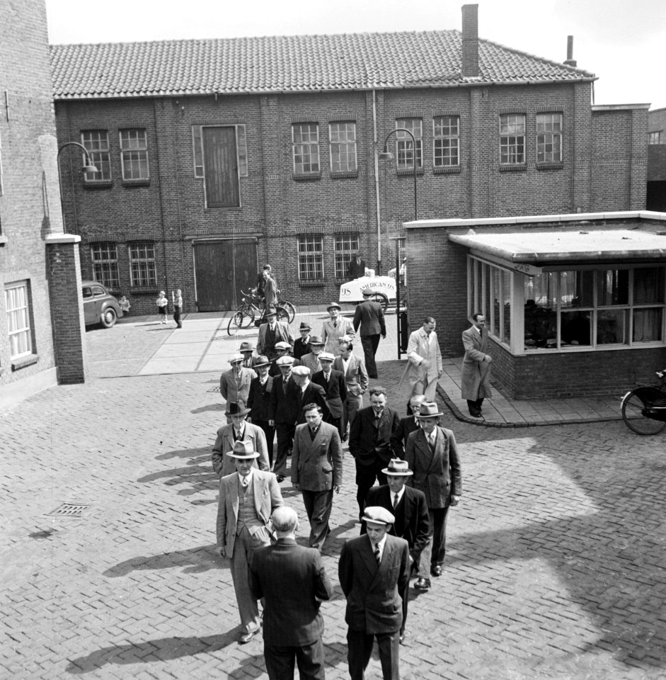 Mannen lopend op fabrieksterrein met een portiersloge, op de achtergrond een ijs, Bestanddeelnr 255-8540