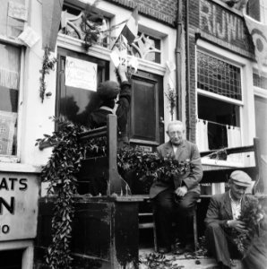 Mannen versieren hun woning in de Jordaan. Op de deur staat aangeplakt Aanmeld, Bestanddeelnr 900-4544
