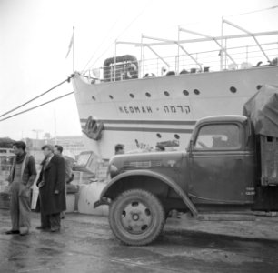 Mensen staand bij een vrachtwagen op een kade op de achtergrond het schip de Ke, Bestanddeelnr 255-0015