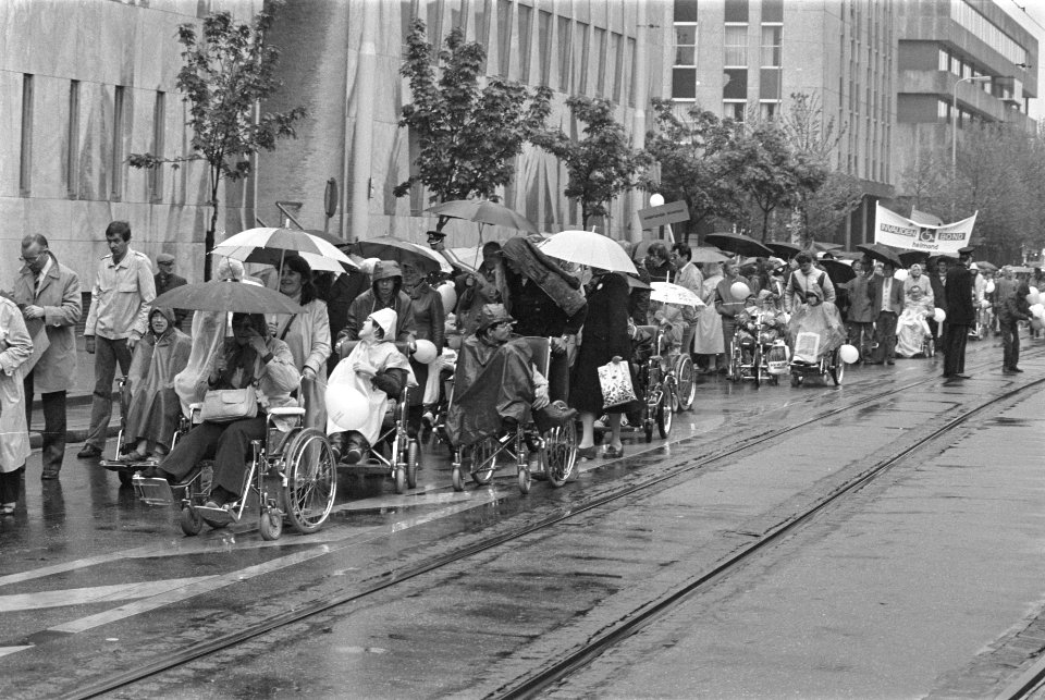 Mensen in rolstoel rijden door de stad, met paraplu's tegen de regen, Bestanddeelnr 932-6029