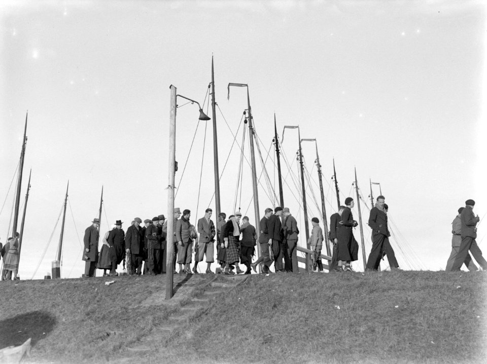 Mensen met schaatsen in de hand op de dijk van Marken met op de achtergrond de m, Bestanddeelnr 189-1077