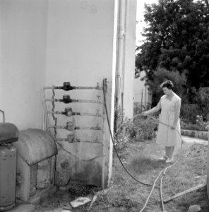 Mevrouw Wagner besproeit haar tuin met een tuinslang die verbonden is met een wa, Bestanddeelnr 255-4827