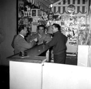 Meester Carletti achter de bar van de school. Aan de muren hangen fotos van ber, Bestanddeelnr 254-0131