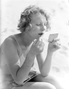 Model Eva Waldschmidt zit in het zand en stift haar lippen, Bestanddeelnr 252-0777