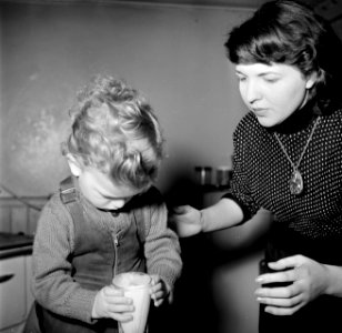 Moeder helpt haar peuter bij het op tafel zetten van een glas melk, Bestanddeelnr 252-9380