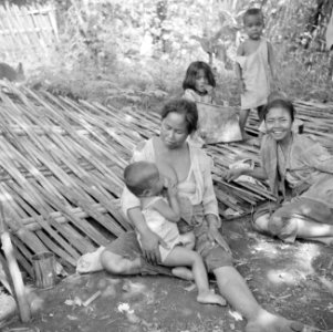 Moeders en kinderen op een gedèk, een wand van gespleten en gevlochten bamboe, Bestanddeelnr 255-6683