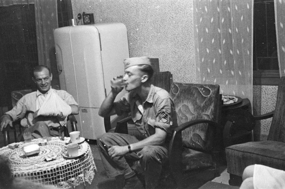 Militairen om salontafel in een huiskamer, één met arm in mitella, Bestanddeelnr 41-4-4