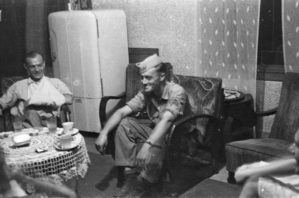 Militairen om salontafel in een huiskamer, één met arm in mitella, Bestanddeelnr 41-4-3