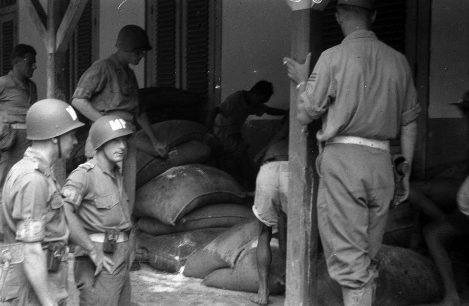 Militaire politiemannen staan bij een stapel balen op een veranda, Bestanddeelnr 3015