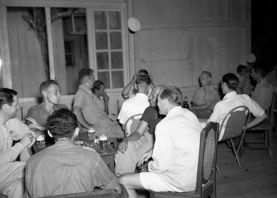 Militairen en mannen in burerkleding zitten in een kantine rond tafels met glaz, Bestanddeelnr 15939